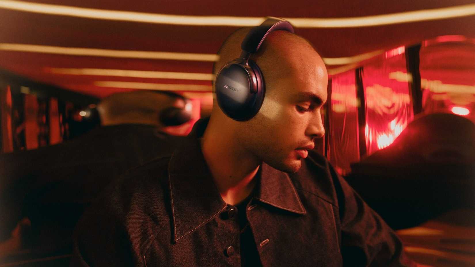 /de/images/bose-2nd-gen-quietcomfort-ultra-headphones-being-worn-by-a-man-in-a-red-room.jpg